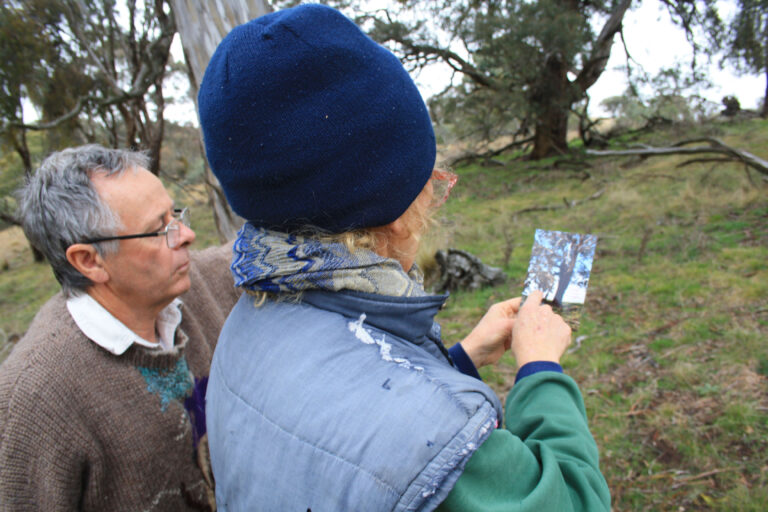 Two people holding a photo of a tree outside.